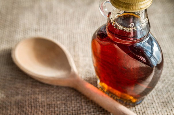 Glass bottle of amber maple syrup with rich color, set on a wooden surface.