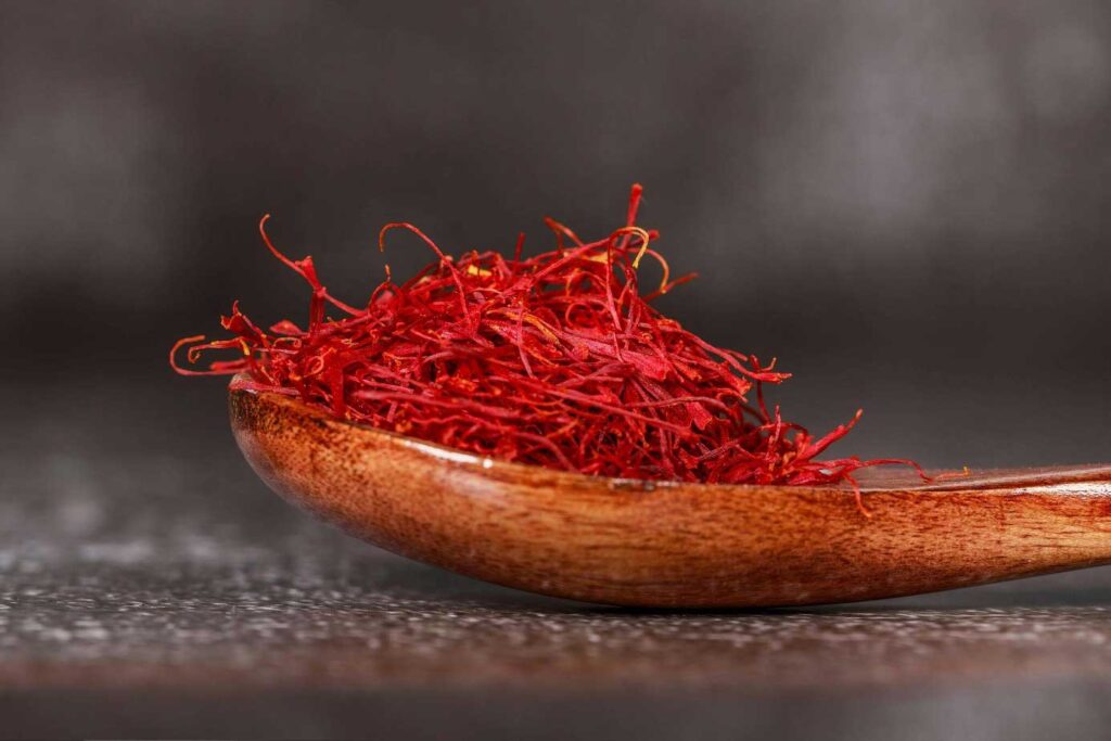 Thin red saffron threads displayed in a small spoon, used as a fragrant spice.