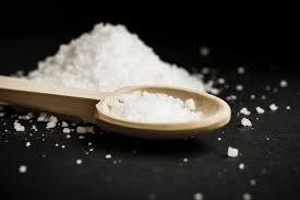Pile of salt next to wooden spoon full of salt.