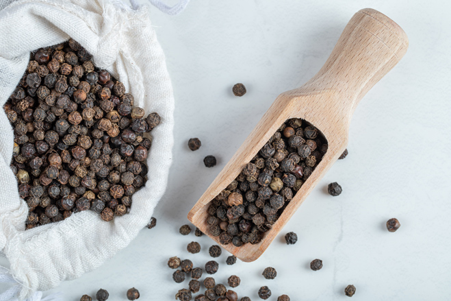 White sack filled with Tellicherry Black Pepper drying on a gray table