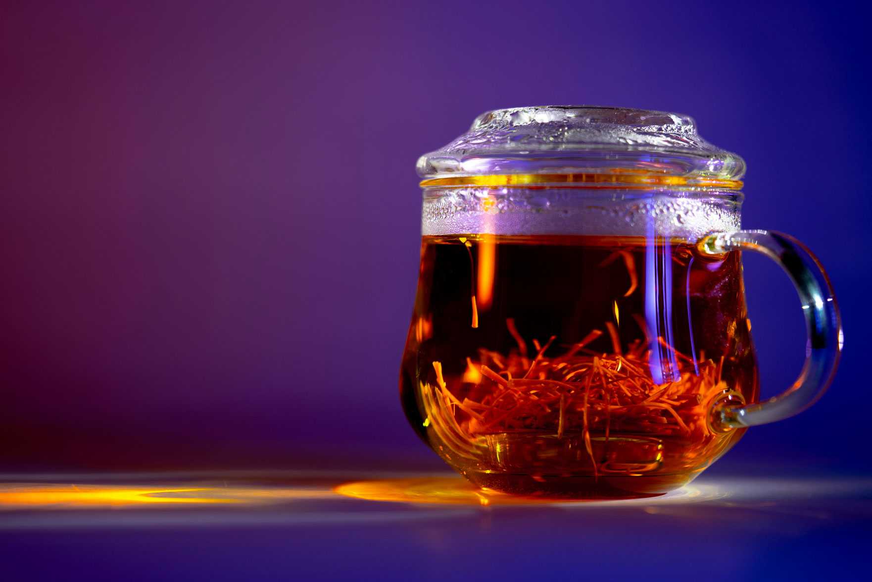 A cup of saffron-infused tea in a clear glass, highlighting the golden spice threads and their vibrant color and aroma.